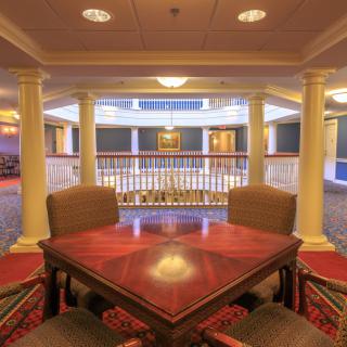 An elegant interior space featuring a wooden table with chairs, surrounded by columns and a carpeted floor.
