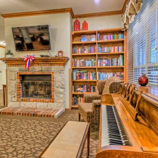 A cozy living room featuring a piano, a fireplace, and bookshelves filled with colorful books.