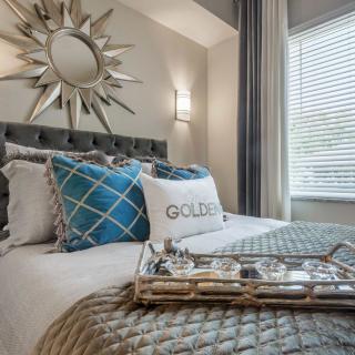 A stylishly decorated bedroom featuring a sunburst mirror, patterned pillows, and a tray on the bed.