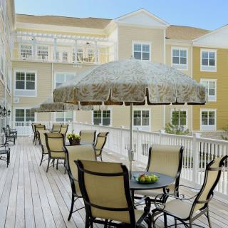 A sunny outdoor patio area with tables, chairs, and umbrellas in front of a building.