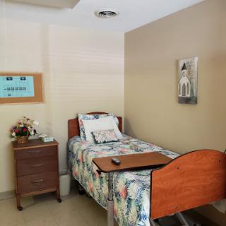 A cozy hospital room featuring a single bed with floral bedding, complemented by a nightstand and decorative wall art.
