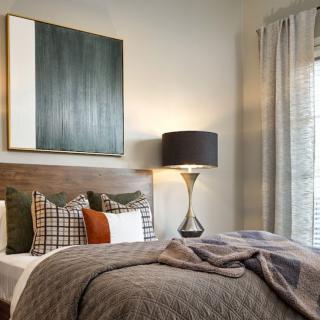 A modern bedroom with stylish decor, featuring a large artwork above the bed, a sleek lamp on the side table, and cozy pillows and comforter.