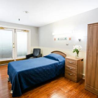 A minimalist bedroom with a single bed, wooden flooring, and simple furniture.