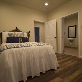 A cozy bedroom with a neatly made bed, featuring an attached bathroom and warm lighting.