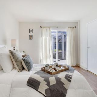 A modern, minimalist bedroom with neutral colors and cozy decor, featuring ample natural light from a sliding glass door.