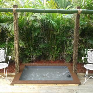 Outdoor hot tub with surrounding tropical plants and bamboo frame.