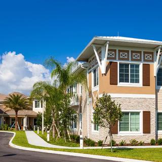 A modern residential building surrounded by palm trees and lush landscaping under a clear blue sky.