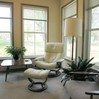 A cozy living room corner with a white armchair, footstool, and large windows.