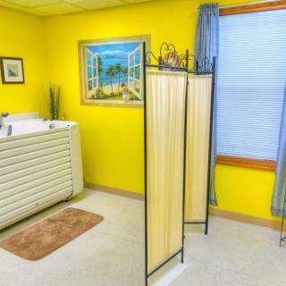 A cozy spa room with bright yellow walls, featuring a massage table and a partition screen for privacy.
