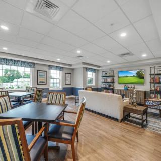 A spacious living area with a dining table, sofa, television, and shelves under bright ceiling lights.