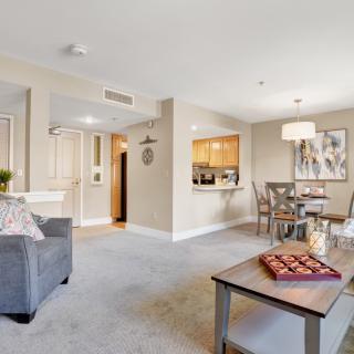 A cozy living room with a sofa, table, and dining area, featuring warm decor and ample lighting.