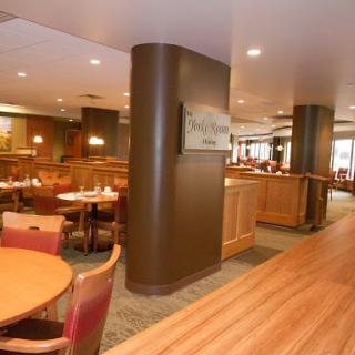 A spacious and warmly lit restaurant interior featuring wooden flooring and comfortable dining arrangements.