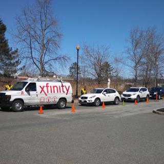 A lineup of vehicles, including an Xfinity service van, parked with traffic cones in a sunny outdoor setting.