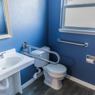 An accessible bathroom with blue walls, featuring a toilet, sink, and grab bars.