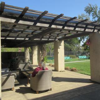 A sunny patio with comfortable outdoor seating under a pergola, overlooking a serene garden area.