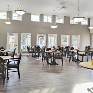 A spacious dining area with multiple tables and chairs, featuring large windows and ceiling lights.