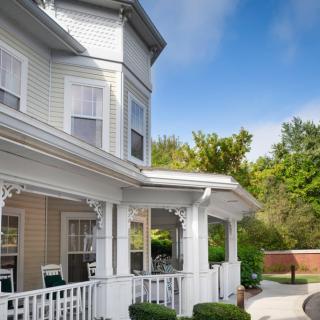 A charming Victorian-style house with a white porch and surrounded by greenery.