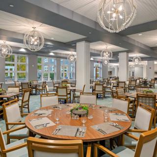 A spacious and modern dining room with elegantly arranged tables and chairs, featuring contemporary lighting fixtures.