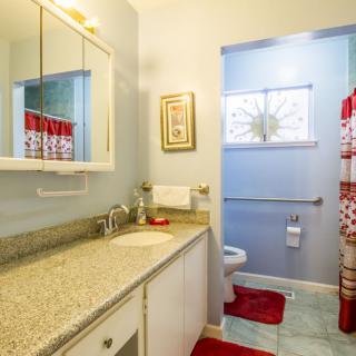A well-lit bathroom with a granite countertop, mirror, and red accents including towels and a shower curtain.