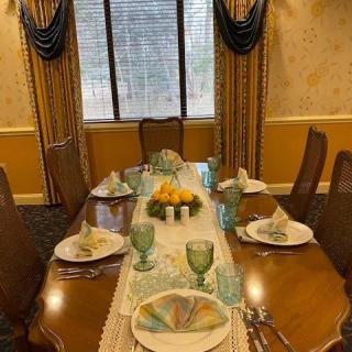 A beautifully set dining table with elegant plates, glassware, and a fruit centerpiece in a formal dining room.