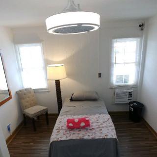 A minimalist bedroom with a single bed, lamp, and chair.