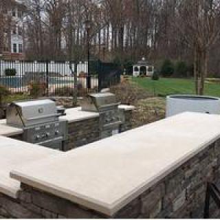 An outdoor kitchen area with grills and stone countertops in a backyard setting.