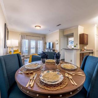 A modern dining area with a round table set for four, featuring elegant tableware and a stylish living space in the background.