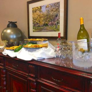 A buffet setup with wine, glasses, and food on a wooden table in an indoor setting.