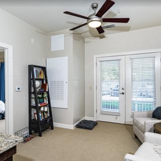 A cozy living room featuring a ceiling fan, bookshelf, and French doors leading outside.