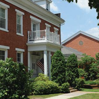 A charming brick house with a front porch and lush garden on a sunny day.