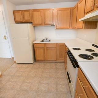 A compact kitchen with wood cabinets, tile flooring, and standard appliances.