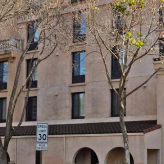 A four-story building with trees in front and a speed limit sign on the street.