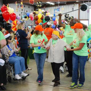 Volunteers assist elderly participants during a lively community celebration filled with colorful decorations and joyful energy.