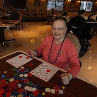 An elderly woman enjoying a game of bingo, surrounded by colorful markers and engaged in a social activity.