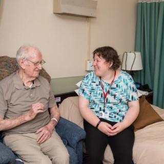 An elderly man and a caregiver having a conversation in a living room setting.