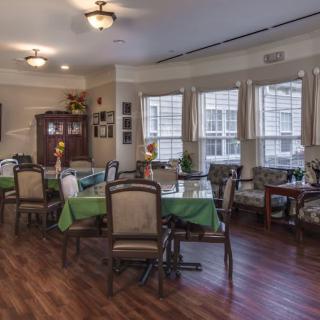 A cozy dining area with several tables and chairs, featuring large windows and hardwood flooring.