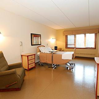 A well-lit hospital patient room featuring a bed, chair, and window.