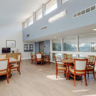 A modern communal dining area with tables and chairs, featuring high ceilings and large windows.