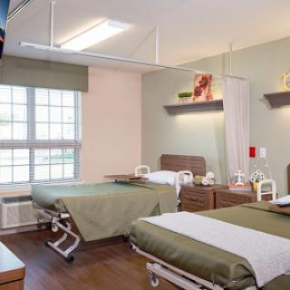 A bright and modern hospital patient room featuring two beds and natural light from a nearby window.