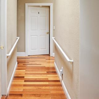 A well-lit hallway with polished wood flooring and a white door at the end.