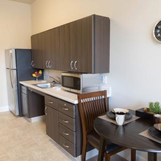 A modern kitchen with dark wood cabinets, a small dining table, and essential appliances.