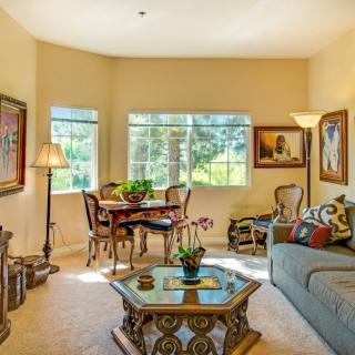 A cozy and elegantly furnished living room with large windows, featuring a sofa, coffee table, dining area, and decorative artworks.