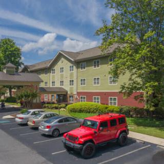 A view of a hotel with a parking lot featuring a red vehicle and surrounded by greenery.