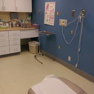 A well-equipped medical examination room featuring a blue wall, various healthcare supplies, and a patient bed.