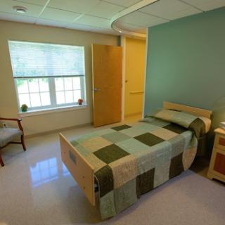 A bright and serene hospital room featuring a single bed, a window allowing natural light, and a simple chair.