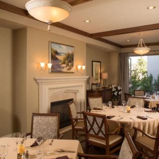 An elegant dining room with neatly arranged tables and chairs, featuring a fireplace and artwork on the wall.
