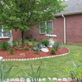 A well-maintained front yard garden featuring a tree, colorful flowers, and brick siding.