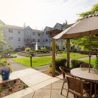 A peaceful garden patio with a fountain, surrounded by a well-kept lawn and situated next to a residential building.