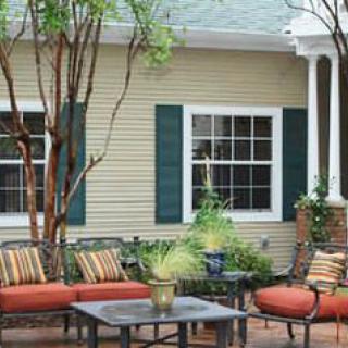 A cozy patio area with outdoor seating in front of a house with green shutters.