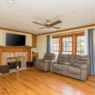 A cozy living room featuring leather couches, a mounted TV, and a fireplace with wooden floors and large windows.